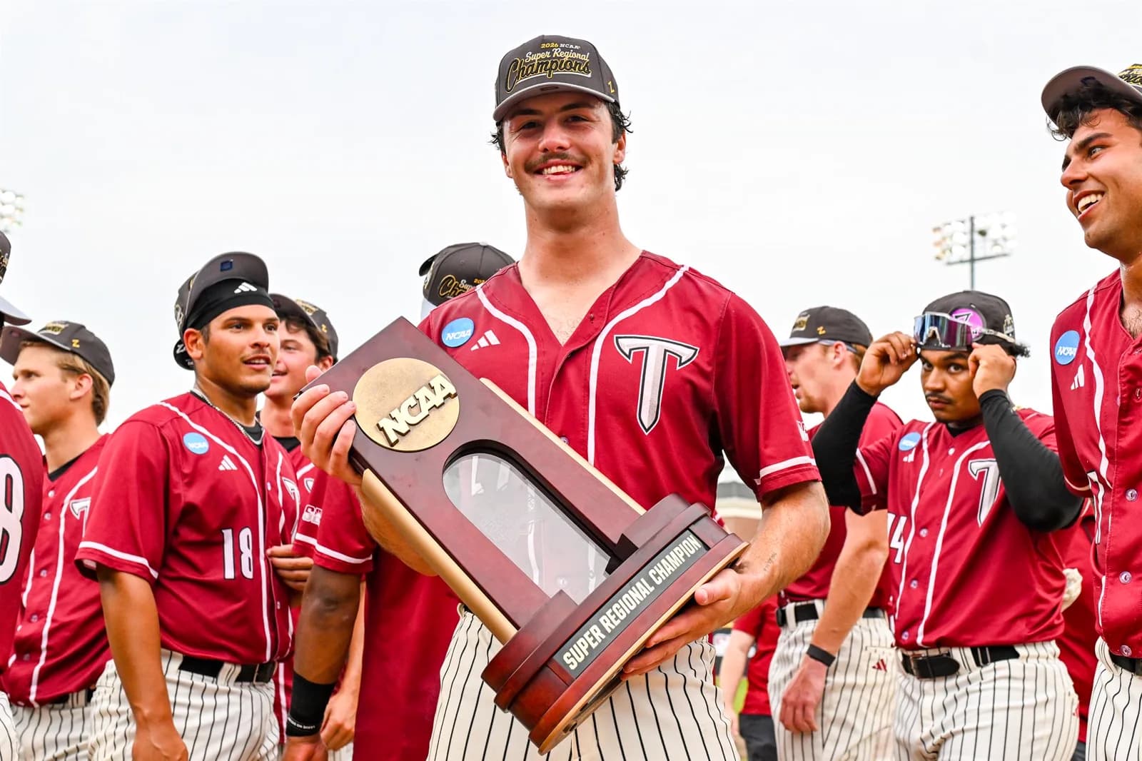 Dylan Alonso holding the NCAA Super Regional Champion trophy with teammates